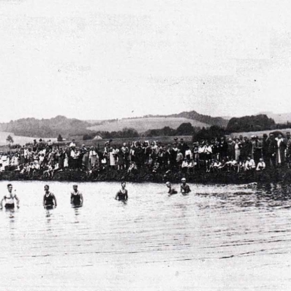 Wettschwimmen im “Strandbad Wahlscheid” in den 1930er Jahren. Am Aggerufer haben sich zahlreiche Zuschauer eingefunden. darunter Parteigrößen und Ortspolizist Grammich.